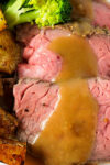 sliced prime rib roast with roast potatoes, gravy and broccoli on plate.