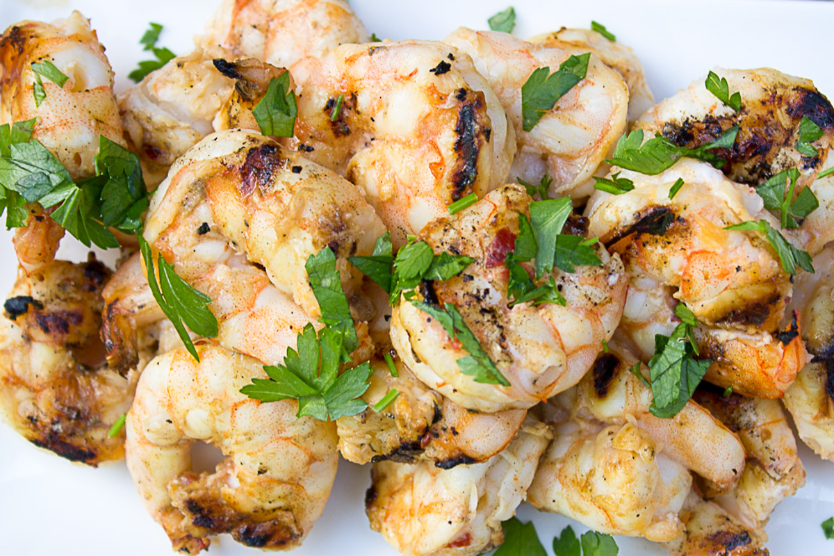 pile of grilled shrimp on white cutting board.