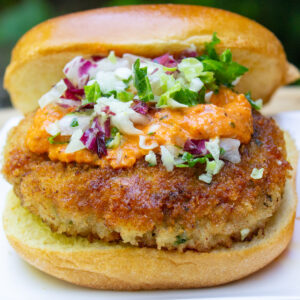 crispy chicken burger on bun with red pepper sauce and coleslaw on top.