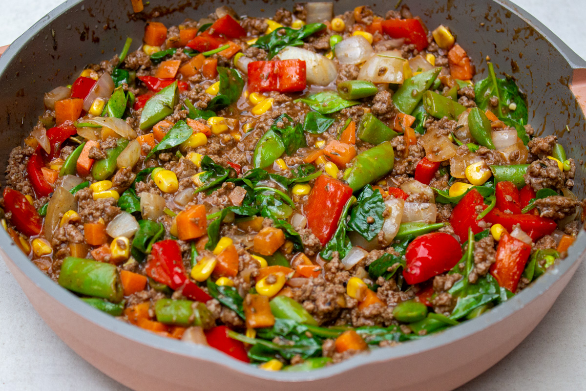 stir fried ground beef and veggies with spinach in skillet.