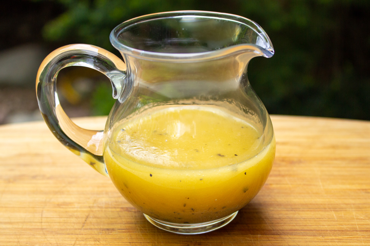 honey lemon dressing in small glass pitcher with pouring spout on table.