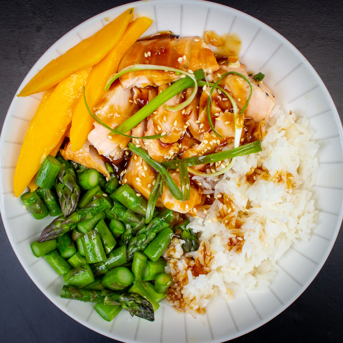 bowl of rice, cut up cooked salmon, asparagus, mango with teriyaki glaze.
