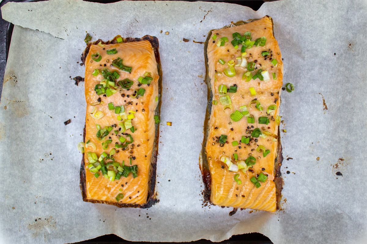 marinated baked salmon filets on lined baking sheet topped with green onions.