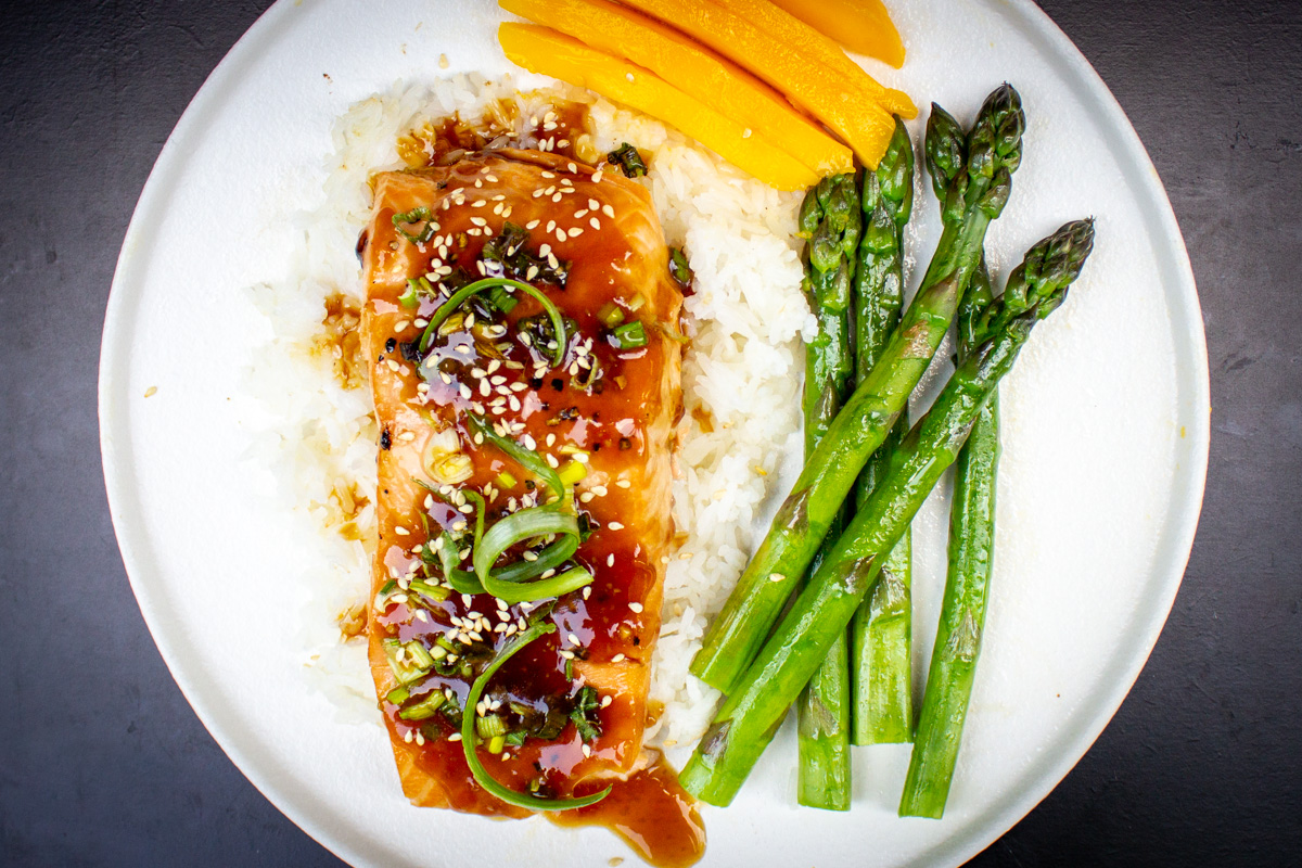 teriyaki glazed salmon over white rice with asparagus and mango on plate.
