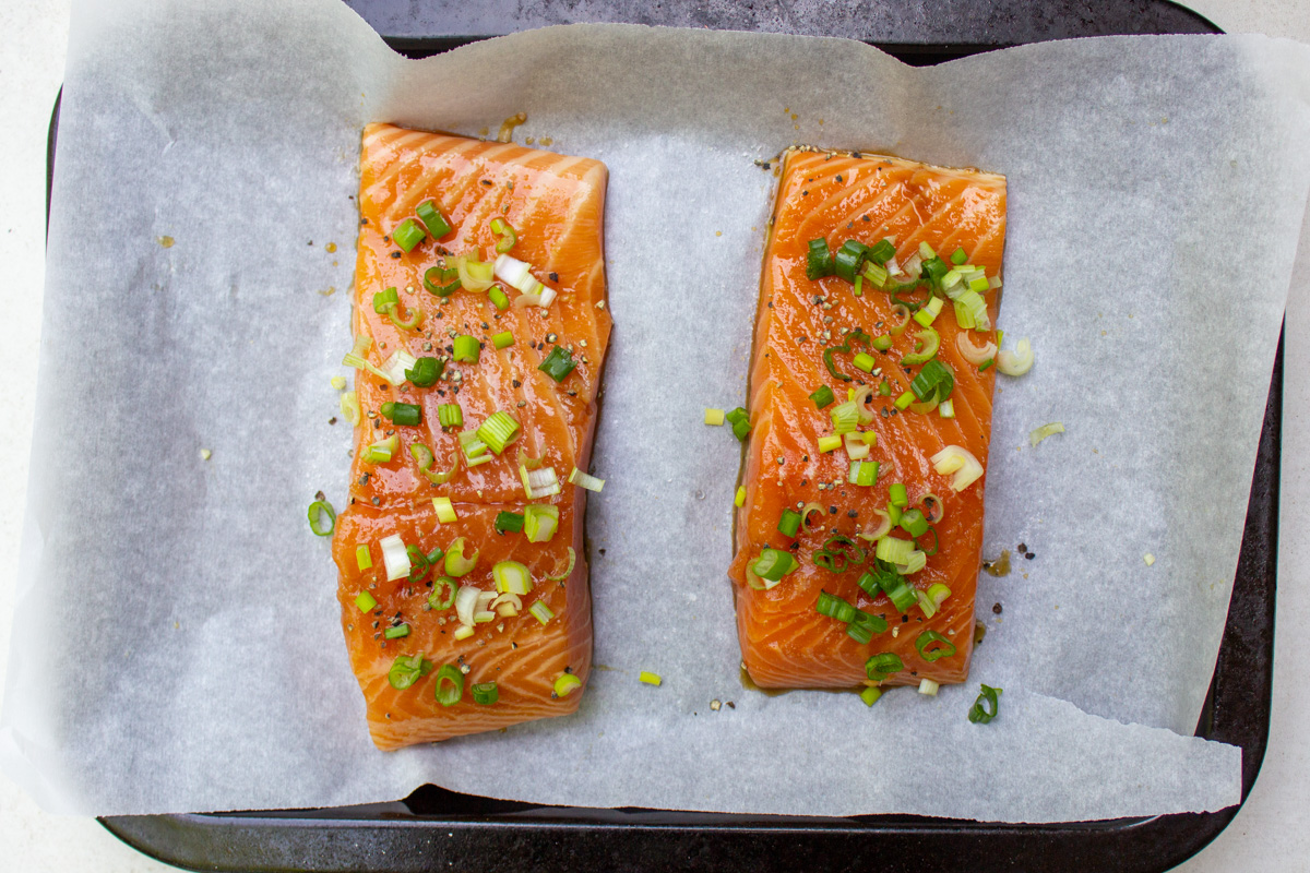 marinated salmon filets on lined baking sheet topped with green onions.