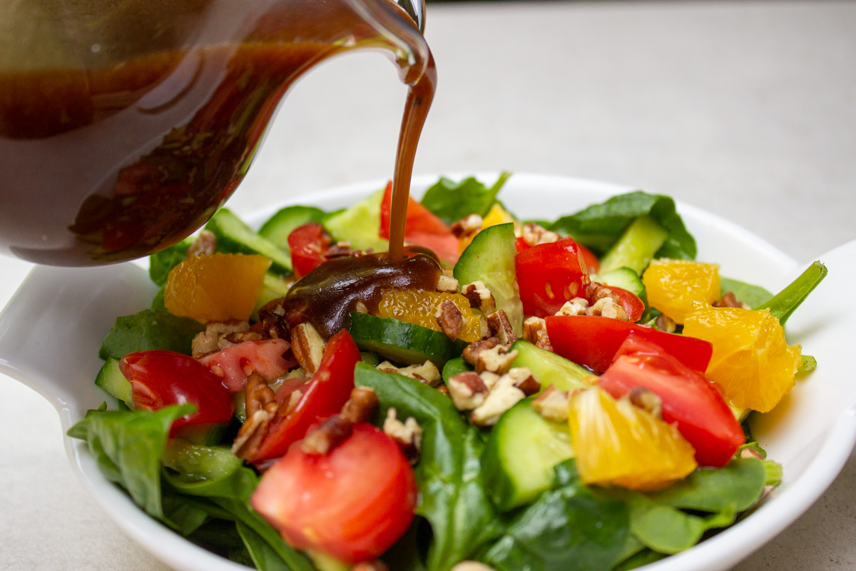 pitcher of maple balsamic dressing pouring onto a bowl of salad.