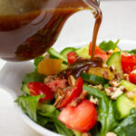 pitcher of maple balsamic dressing pouring onto a bowl of salad.