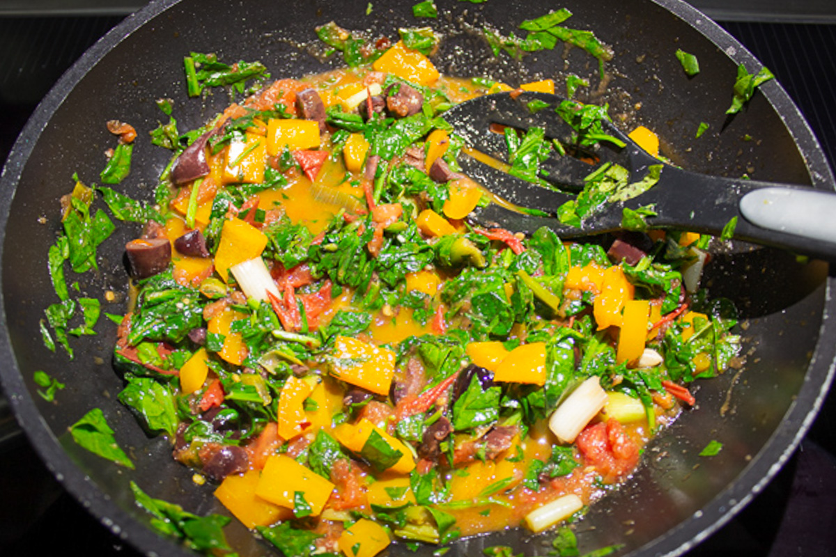 sauteed vegetable sauce in skillet with spinach added.