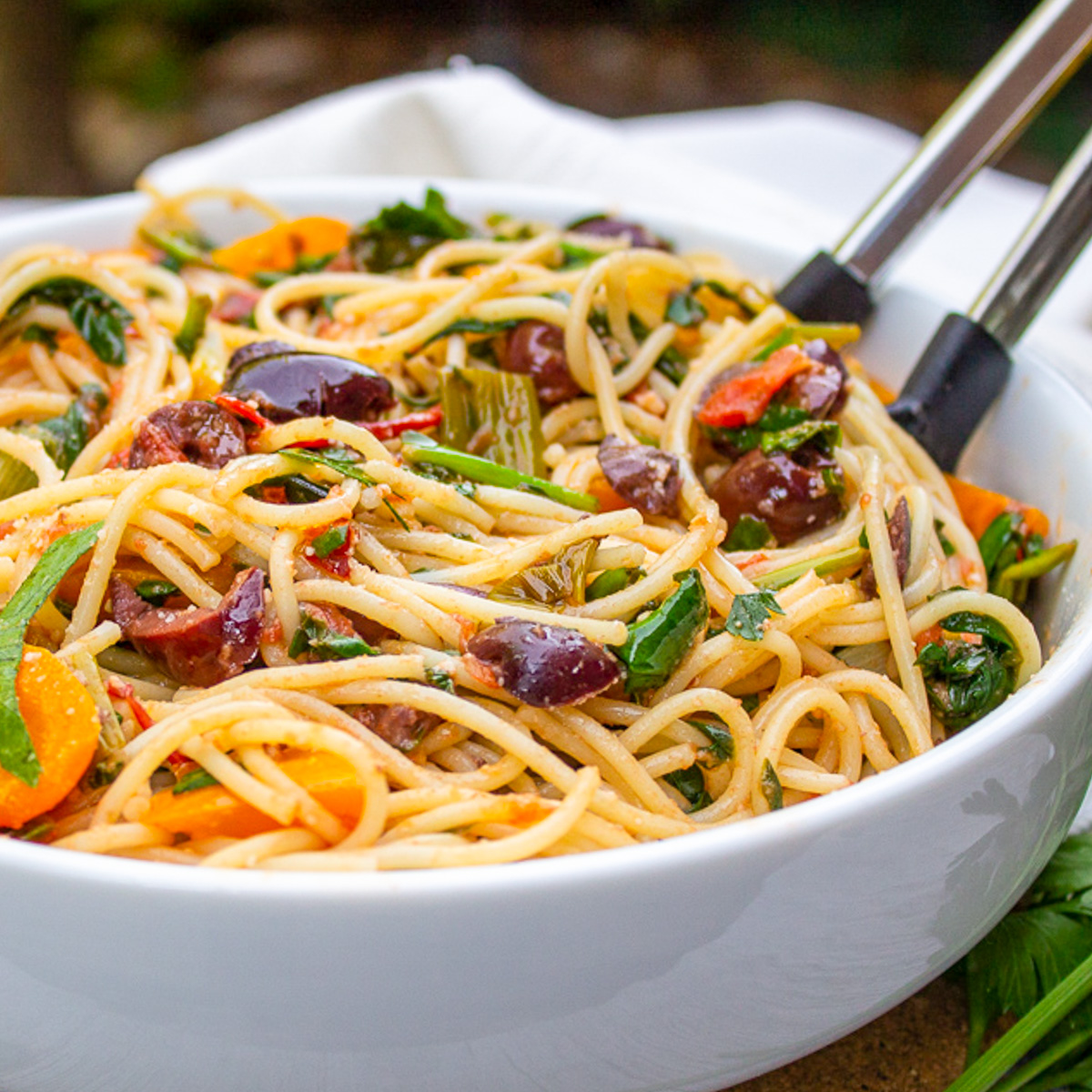 Mediterranean spaghetti in a white bowl on wood table.