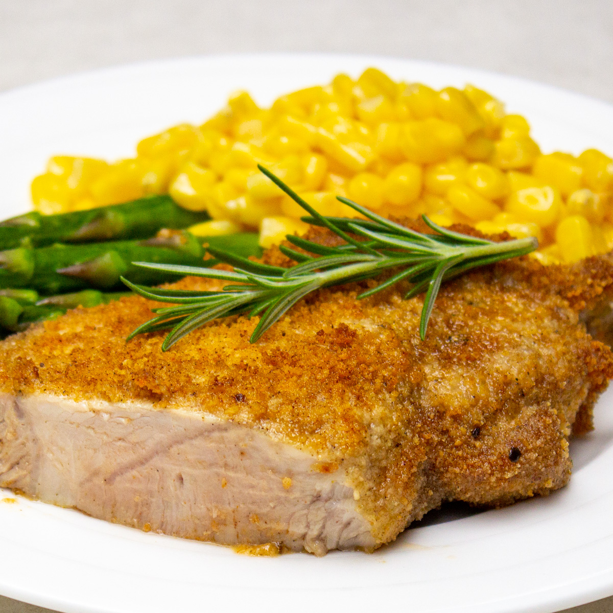 one shake and baked pork chop on plate with corn and asparagus.