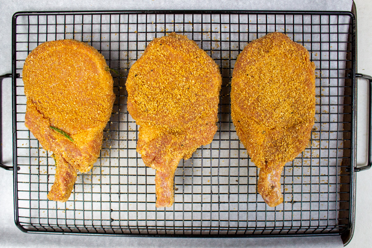 breaded pork chops on wire rack over sheet pan.