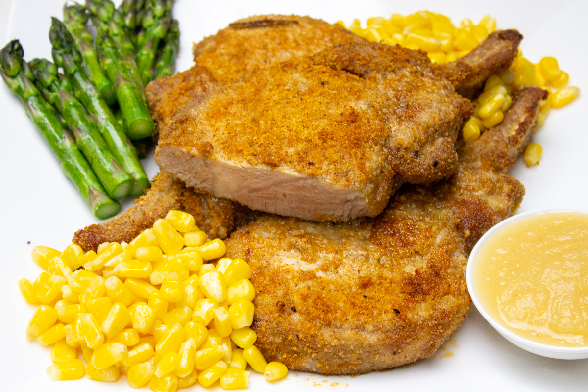 shake and baked pork chops on plate with corn and asparagus.