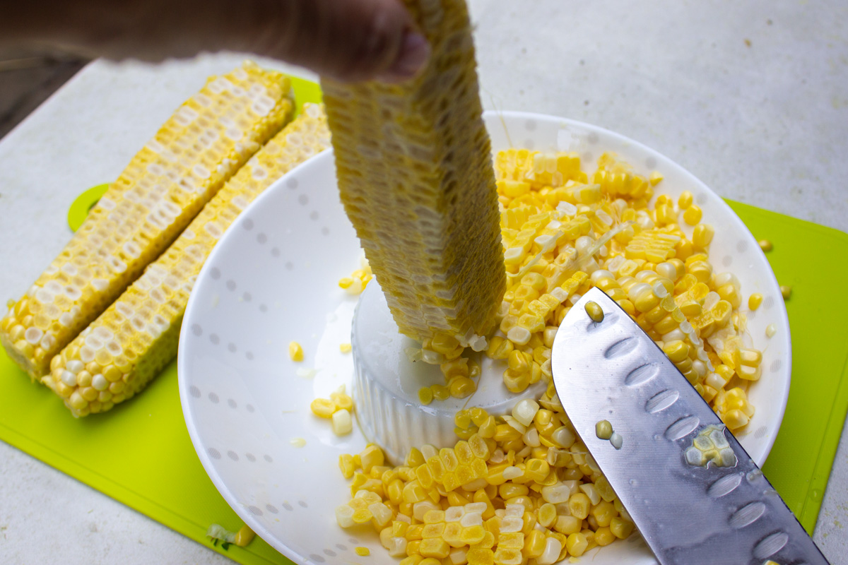 slicing kernels off corn cobs onto a bowl.