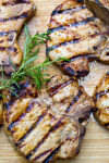 grilled marinated pork chops laying on cutting board with rosemary sprig.