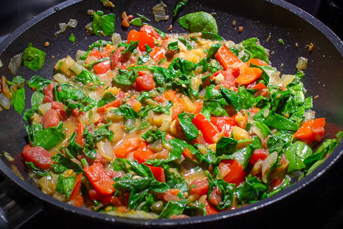 saucy vegetables with capers and spinach in skillet.