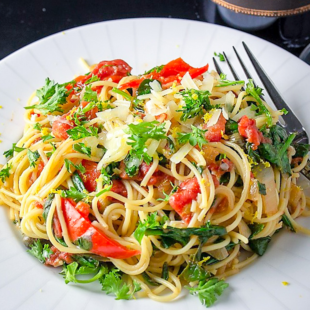 vegetable spaghetti on white plate with wine behind plate.