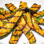 grilled seasoned zucchini slices heaped on white plate.