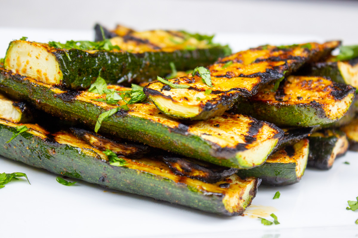 grilled seasoned zucchini slices layered on white plate.