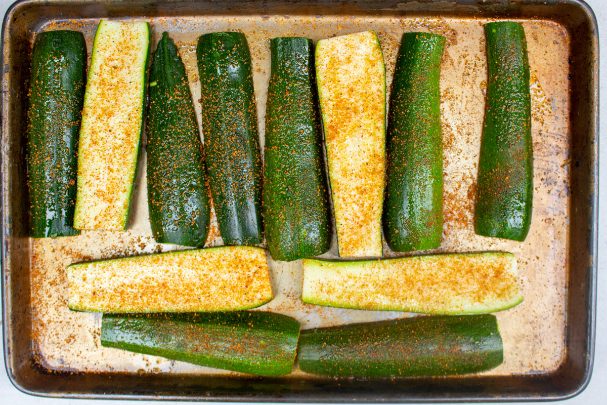 raw seasoned zucchini slices on baking sheet.