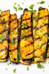 grilled seasoned zucchini slices lined on white plate.