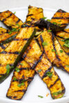 grilled seasoned zucchini slices heaped on white plate.