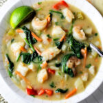 thai style shrimp soup in bowl with spinach and veggies and a lime wedge.