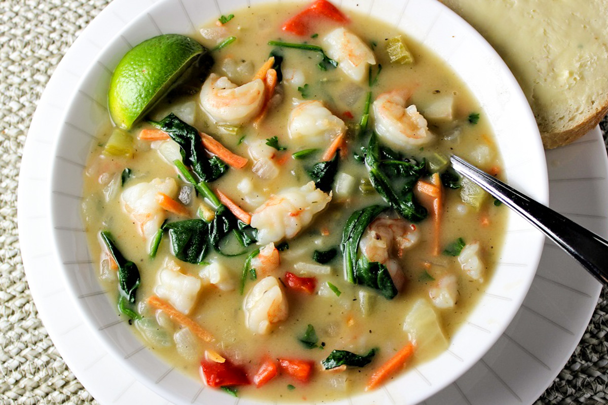 thai style shrimp soup in bowl with spinach and veggies and a lime wedge.