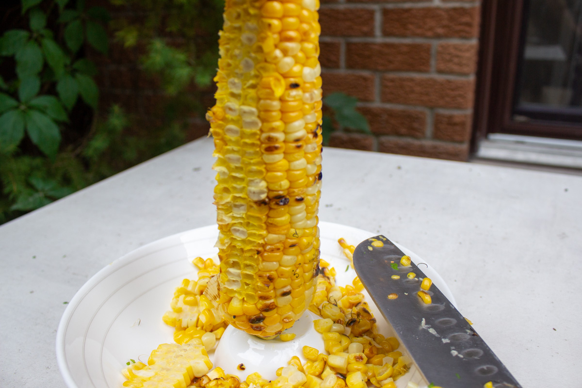 one cob of grilled corn with kernels cut into a bowl.