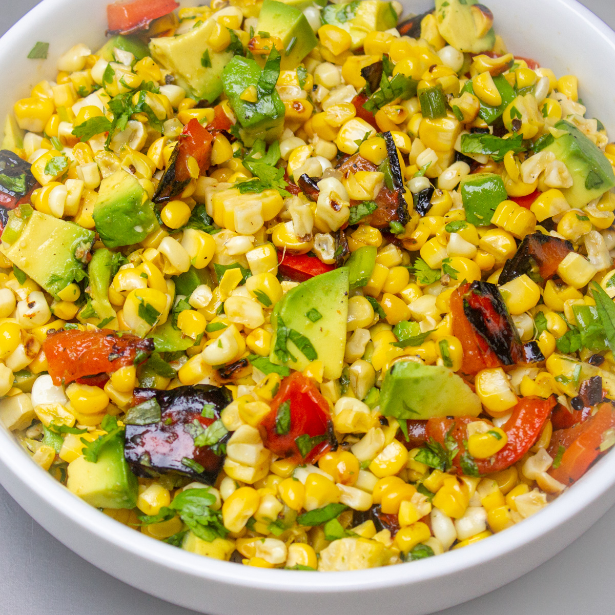 charred corn salad in a white bowl garnished with cilantro.