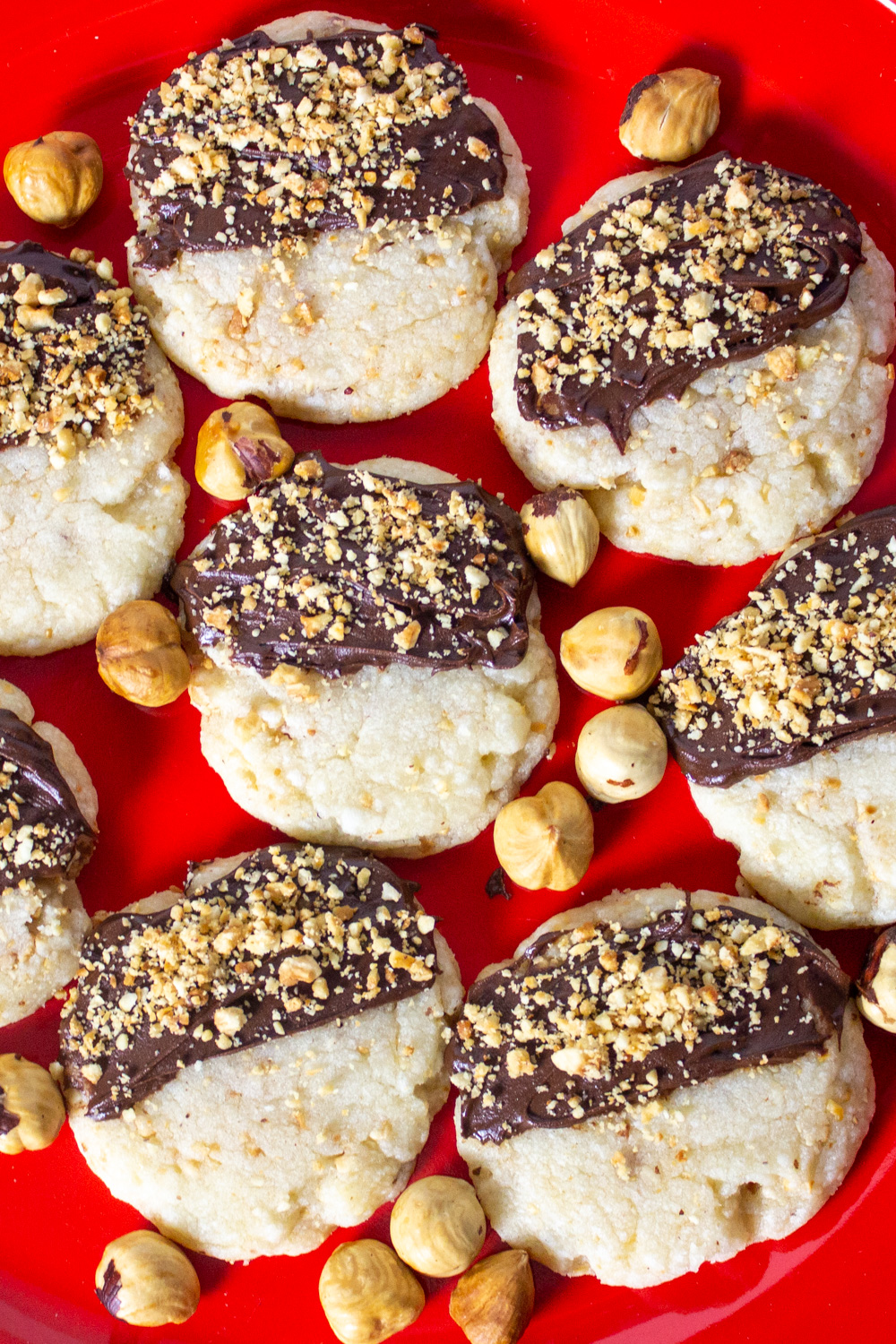hazelnut cookies with chocolate and crushed hazelnuts on red plate.