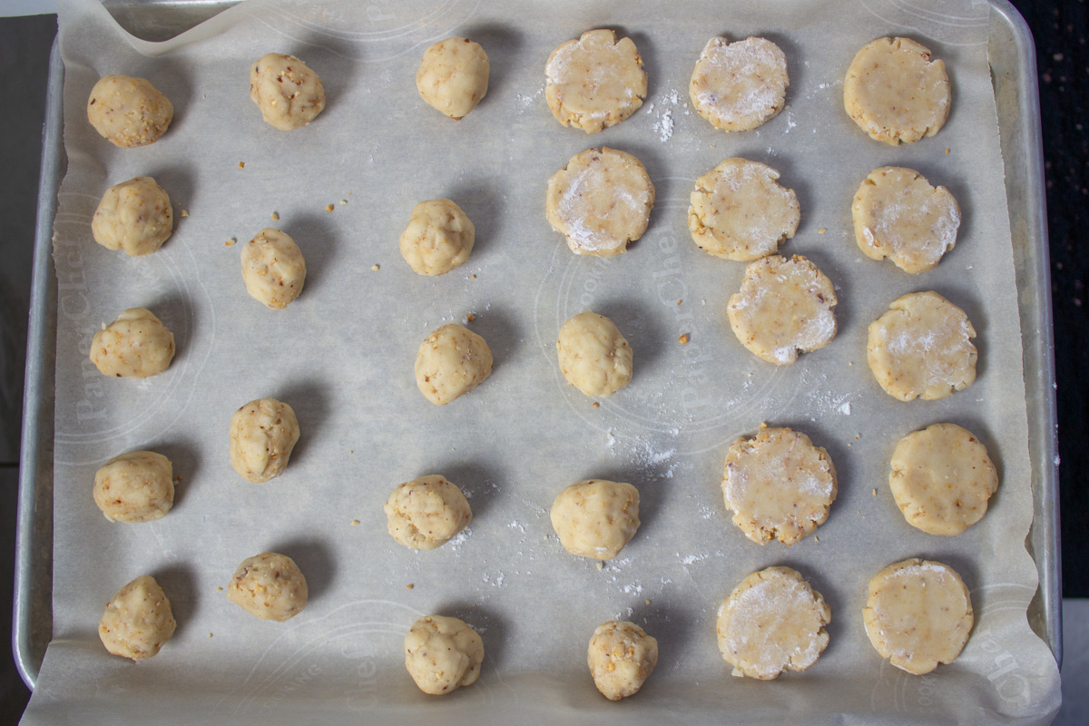 balls of cookie dough, half of them pressed flat on cookie sheet.
