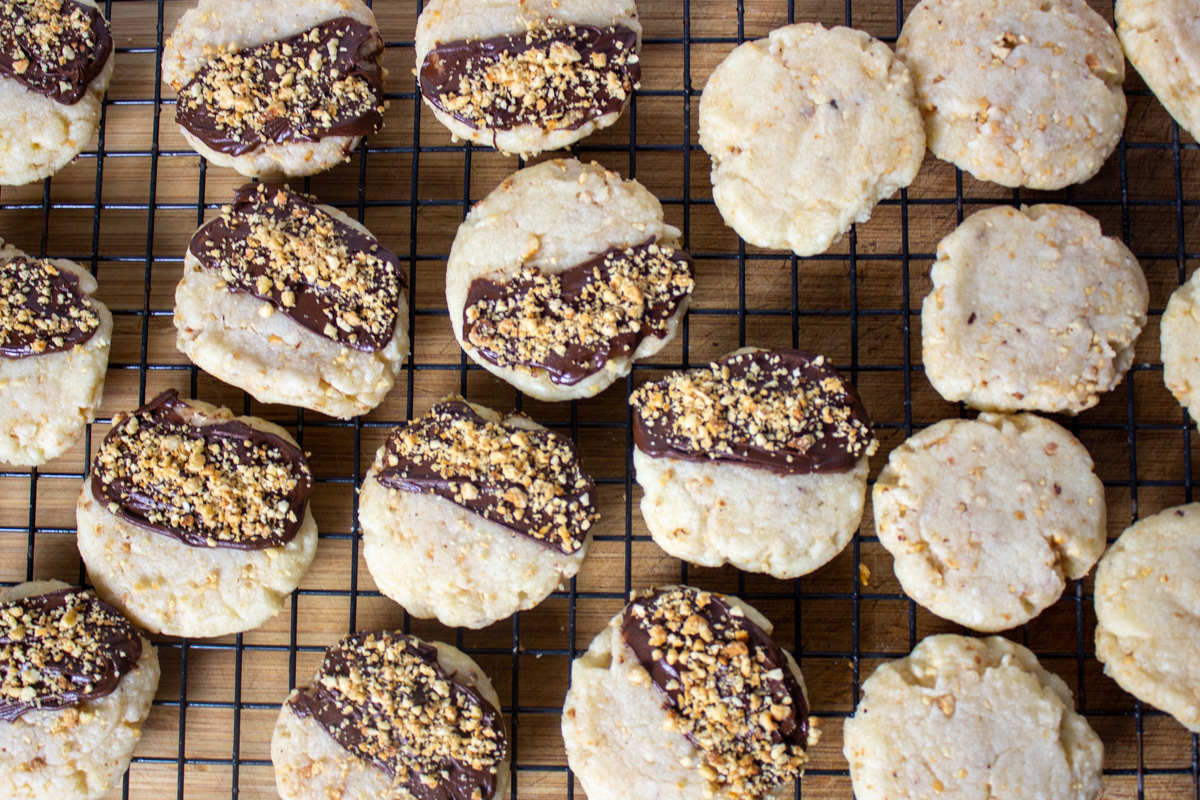 hazelnut cookies, half plain and half with chocolate and crushed hazelnuts on wire rack.