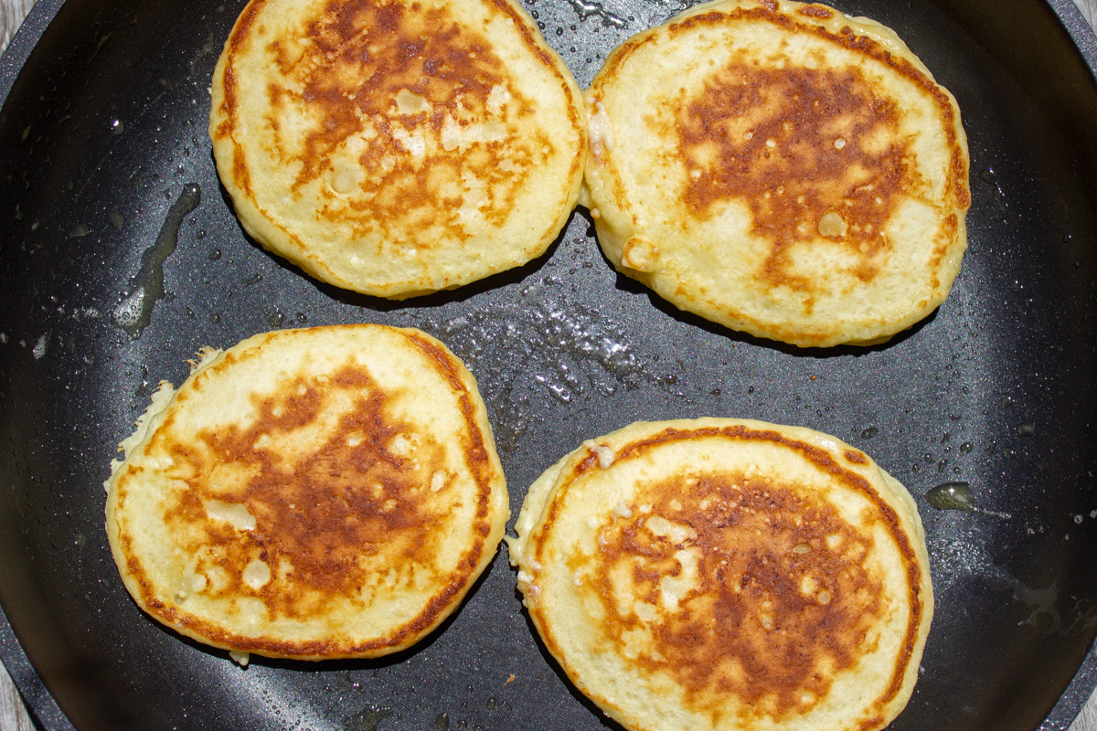4 pancakes cooking in skillet.