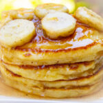 stack of ricotta pancakes with caramelized bananas on top on a plate.