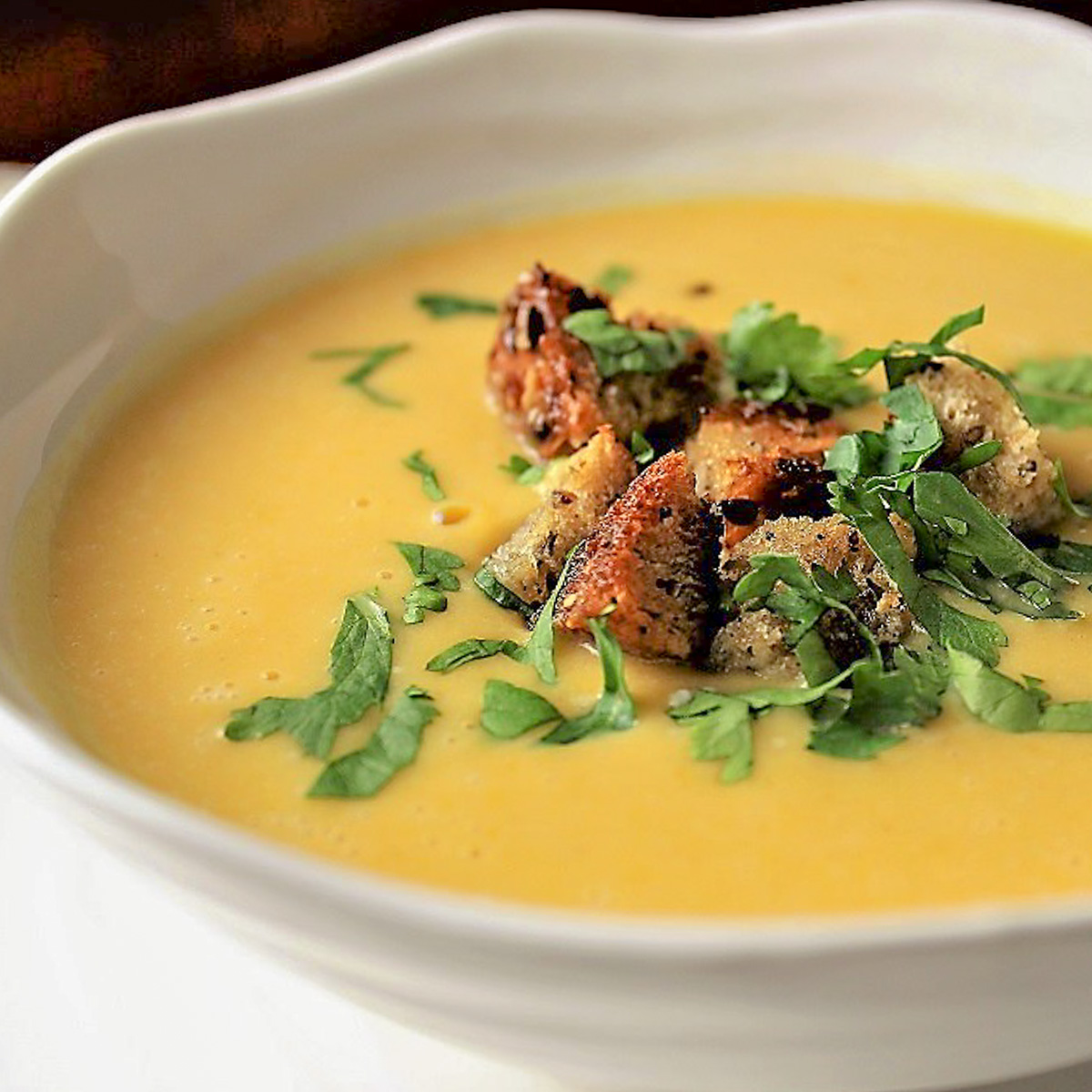spiced butternut squash soup with crouton and cilantro garnish in bowl. 