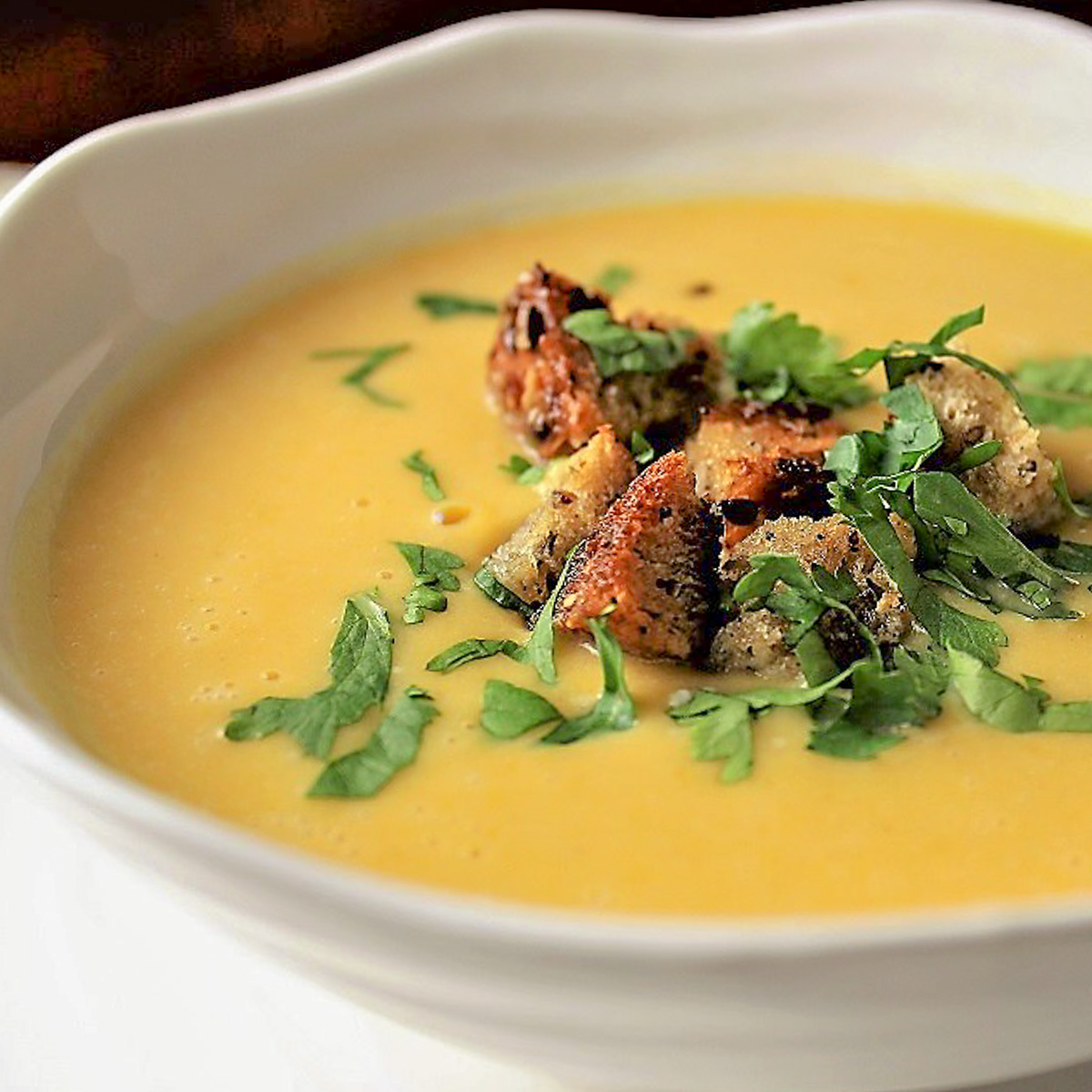 spiced butternut squash soup with crouton and cilantro garnish in bowl.