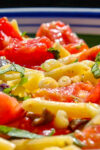 close up of tomato basil pasta with olives and lemon in serving bowl.