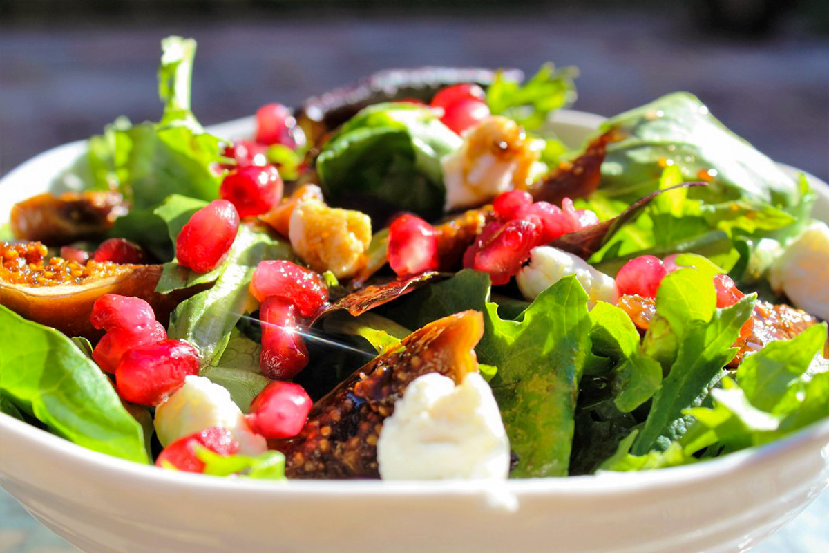 fig salad in bowl with pomegranates and avocado and goat cheese on top.
