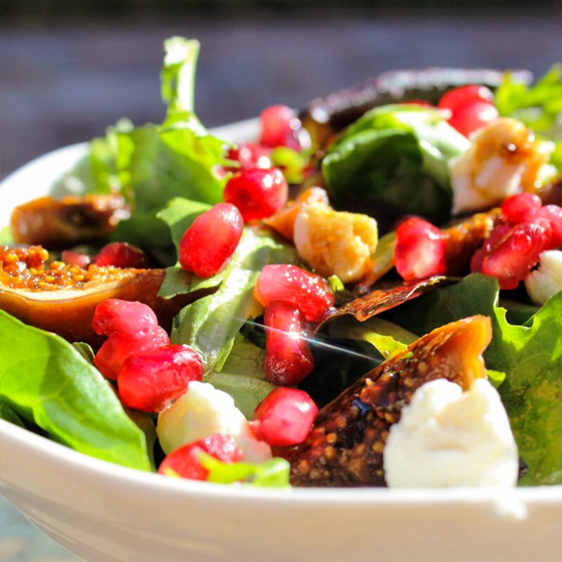 fig salad in bowl with pomegranates and avocado and goat cheese on top.
