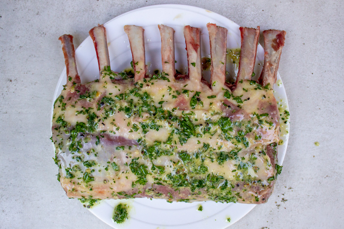 raw rack of lamb coated with herb marinade on plate.