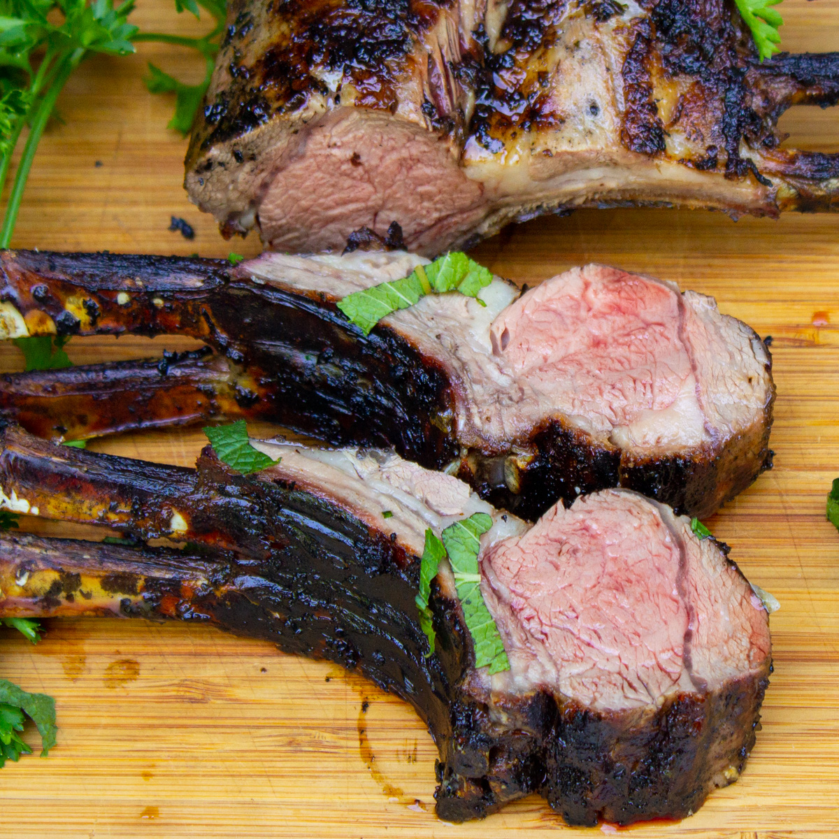 two sliced double lamb chops beside rest of rack of lamb on cutting board.
