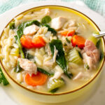 lemon orzo soup with chicken, veggies and coconut milk in yellow bowl.