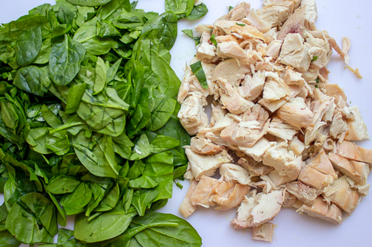 chopped rotisserie chicken and chopped baby spinach on cutting board.