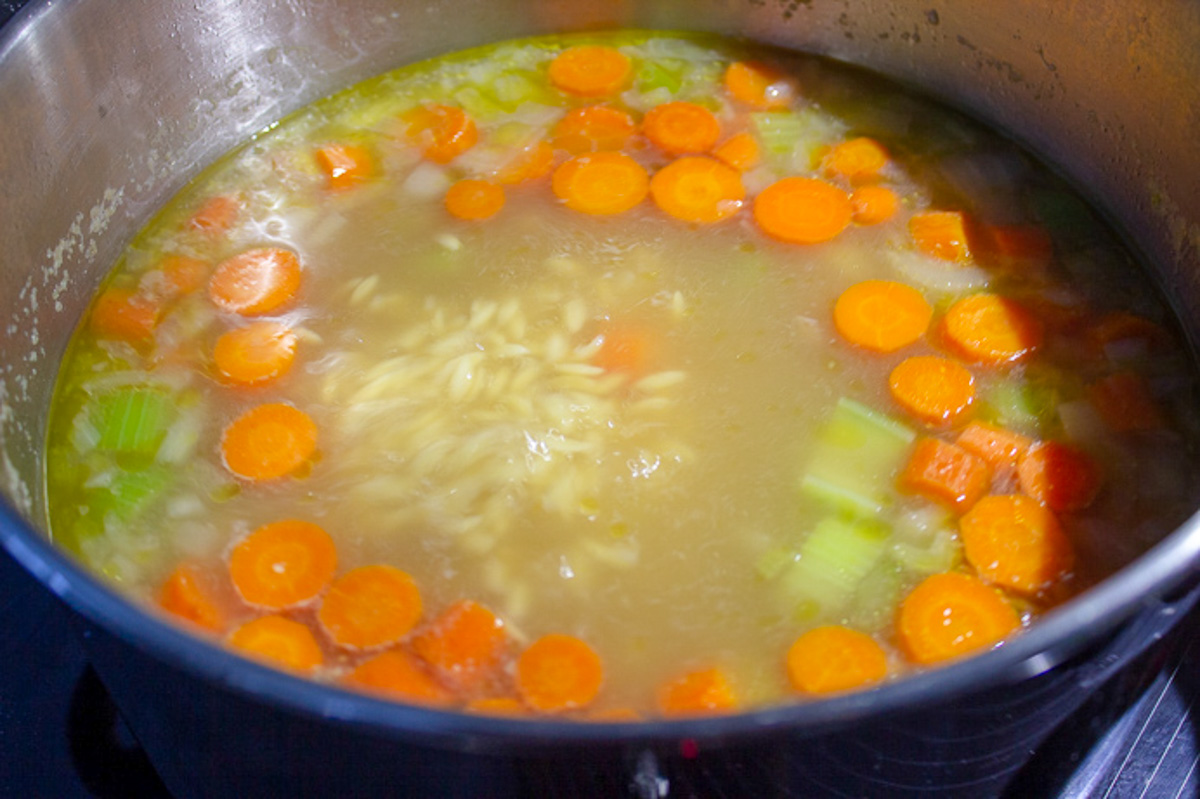 soup with broth, orzo and veggies in pot.