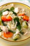 lemon orzo soup with chicken, veggies and coconut milk in yellow bowl.