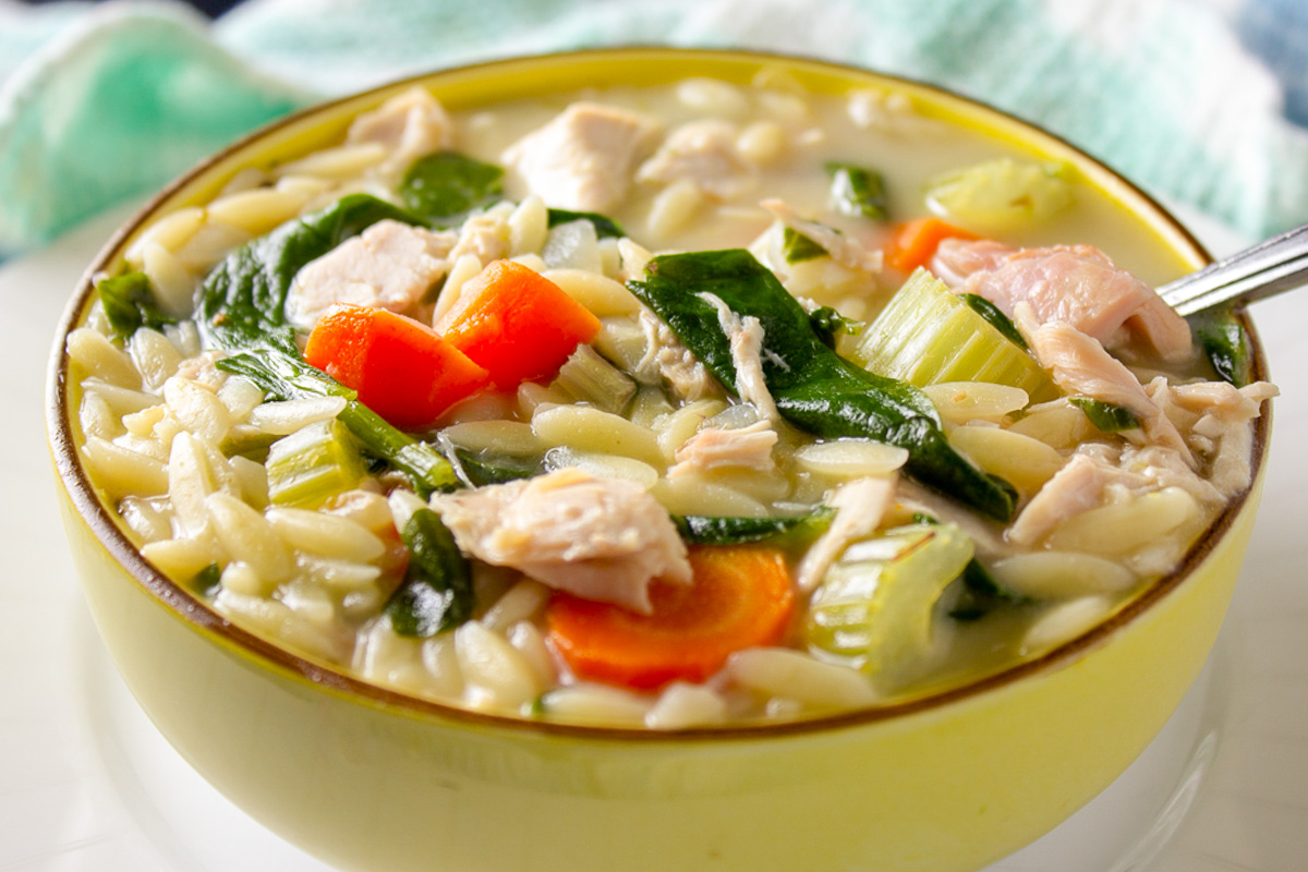 lemon orzo soup with chicken and veggies in yellow bowl.