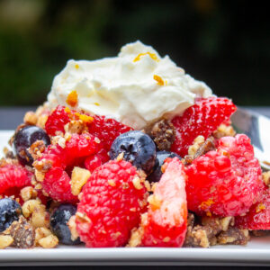 berries with nut mixture topped with whipped cream on plate.