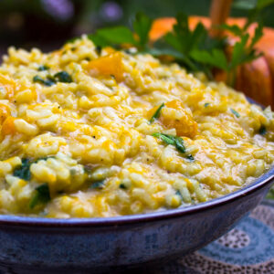 pumpkin risotto in bowl with pumpkin behind it.