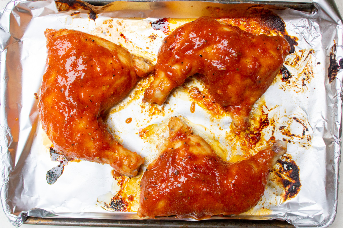 partially baked chicken leg quarters on baking pan with added glaze.