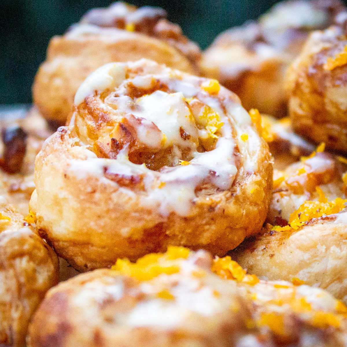 glazed mini puff pastry cinnamon rolls piled on plate.